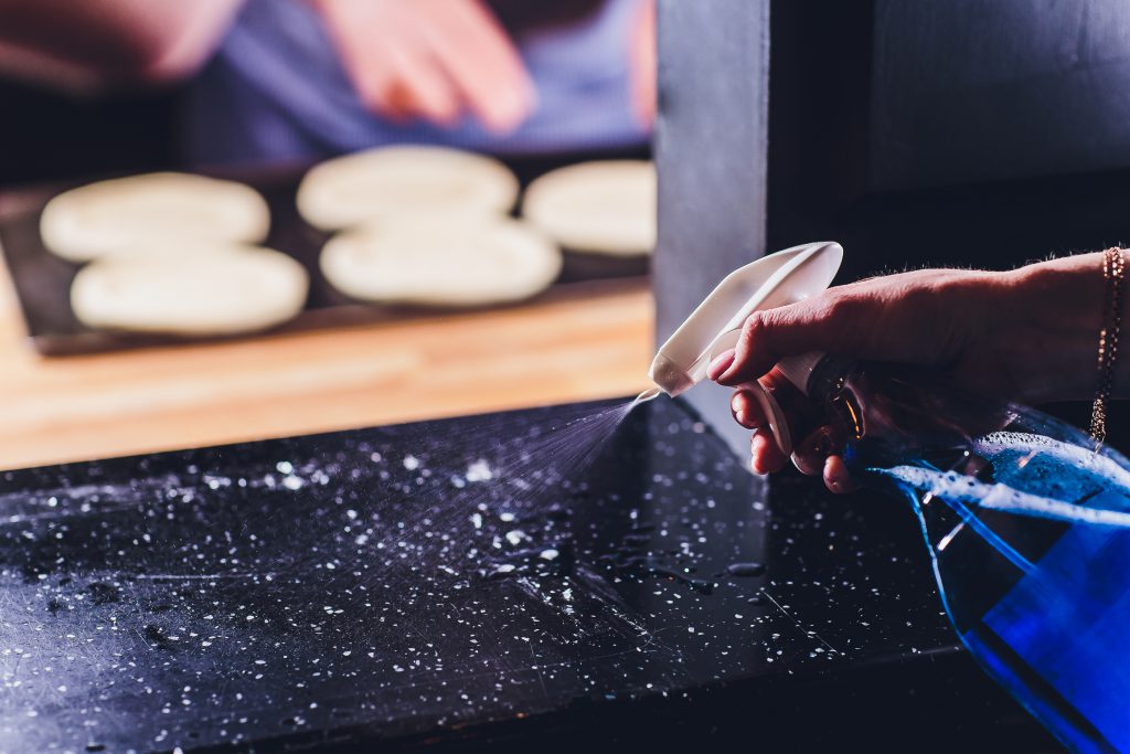 Waiter Cleaning The Table With Disinfectant Spray In Restaurant